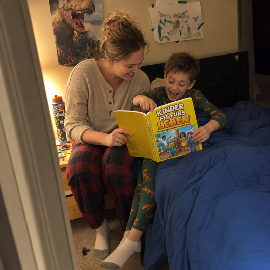 Illustrative Szene: Mutter und Kind lesen das deutsche Comicbuch im Bett